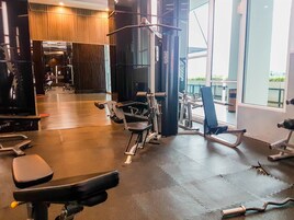 A gym with various exercise equipment, including treadmills and weight machines, and large windows offering views of the outside.