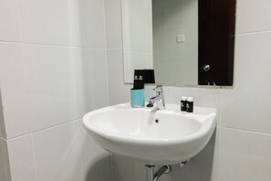 Un lavabo blanc dans une salle de bain, avec un miroir au-dessus, un distributeur de serviettes et deux petits flacons posés sur le lavabo.