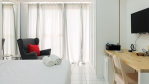 Ein Hotelzimmer mit Bett, Schreibtisch, Stuhl, Fernseher und einem Fenster mit Vorhängen.