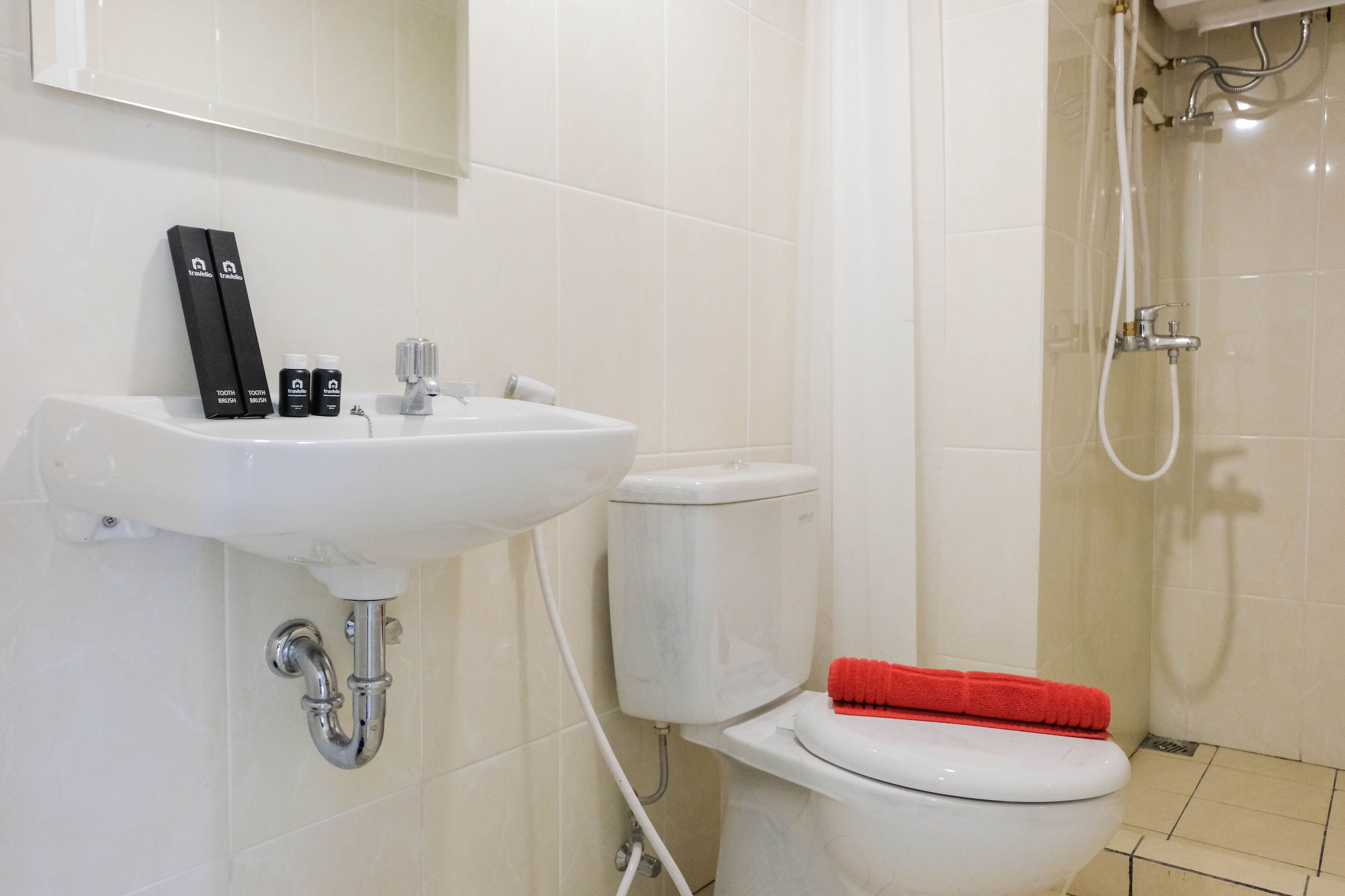 A bathroom with a white sink, toilet, and shower. There are toiletries on the sink and a red bath mat on the toilet.