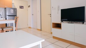 A modern kitchen with a refrigerator, a dining table with chairs, and a television on a cabinet. - Comfortable 2BR Apartment Serpong M-Town Residence (Gading Serpong)