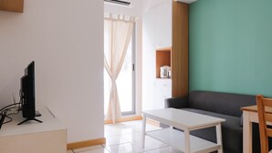 A modern living room with a flat-screen TV on a white stand, a white table, a grey sofa, and a wooden cabinet with a kettle. - Comfortable 2BR Apartment Serpong M-Town Residence (Gading Serpong)