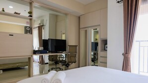 Ein Hotelzimmer mit einem Bett, einem Schreibtisch mit Computer, einem Sessel und einem Fernseher.