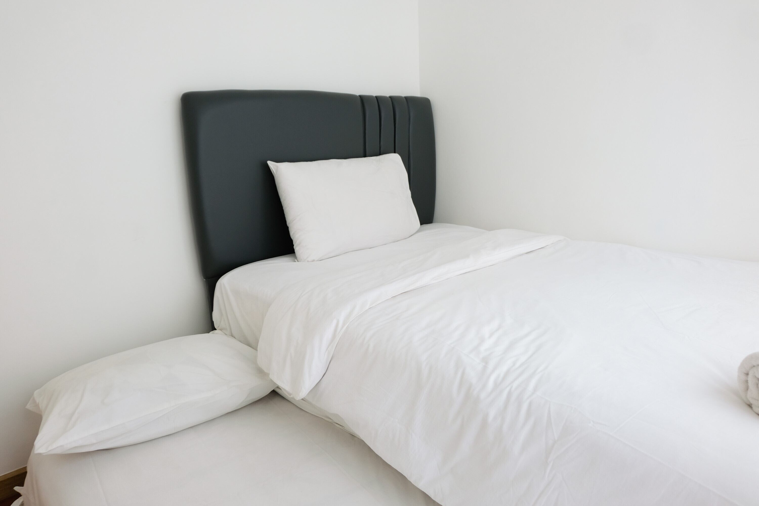 A neatly made bed with white bedding and a dark headboard.