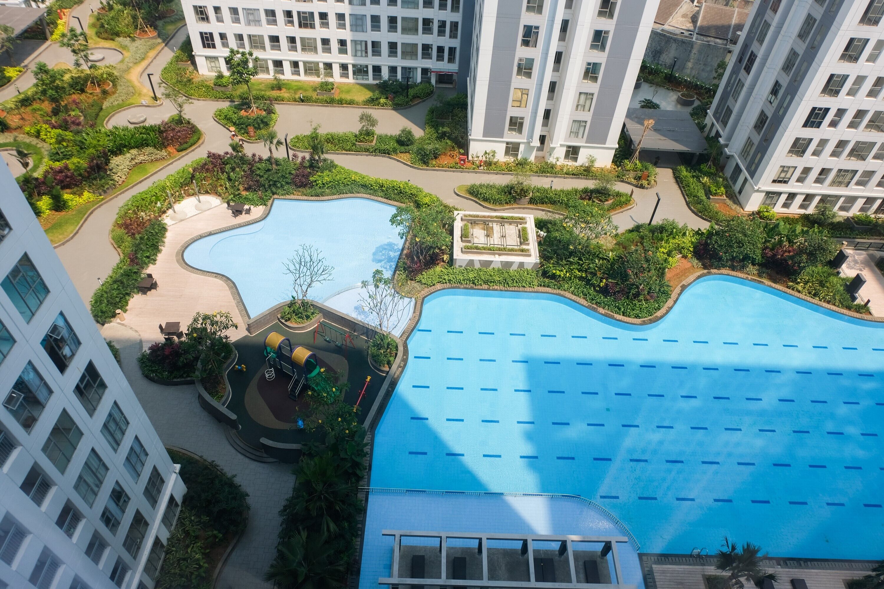 Una gran piscina rodeada de jardines y senderos ajardinados, con edificios altos al fondo.