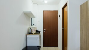 A small kitchenette with a refrigerator, a coffee maker, and a microwave. There is a wooden door and a black cabinet. - Studio near Bella Terra Mall at Tifolia Apartment (Jakarta)