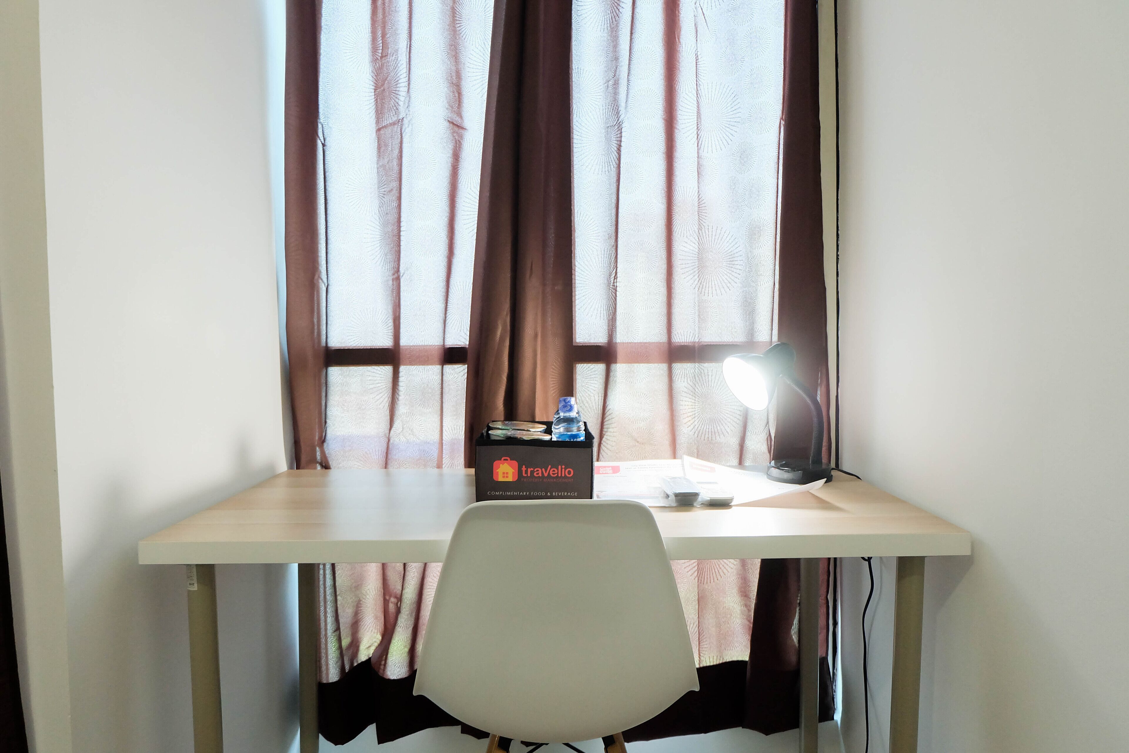 A desk with a chair, a box labeled 'travelio', a bottle, and a lamp.