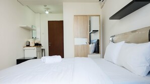 A hotel room with a bed, a desk with a kettle, a mirror, and a wardrobe. - Studio near Bella Terra Mall at Tifolia Apartment (Jakarta)