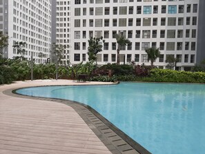 Relax by the serene pool surrounded by lush greenery and a modern building.
