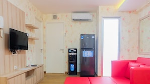 Ein Zimmer mit einem Holzerreptionstresen, einem Flachbildfernseher, einem Wasserspender, einem Kühlschrank und einem roten Sofa.