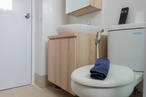 Kylpyhuone, jossa on valkoinen wc-istuin, puinen kaappi ja valkoinen pesuallas.