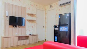 Ein Zimmer mit einem an einer Holzwand montierten Flachbildfernseher, einer eingebauten Unterhaltungseinheit, einem roten Sofa, einem schwarzen Kühlschrank und einem Wasserspender.