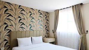Ein Hotelzimmer mit einem großen Bett, einem Nachttisch, einer Wand mit Blättermotiv und einem Fenster mit Vorhängen.