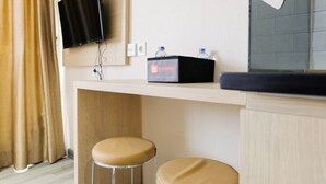 Ein Hotelzimmer mit einem an der Wand befestigten Flachbildfernseher, einer Minibar mit dem Reise-Logo travelio und zwei runden Hocker.