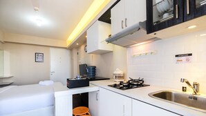 A compact hotel room with a kitchenette, a bed, and a small seating area with stools. - Newly Furnished Studio at Bassura City Apartment (Jakarta)