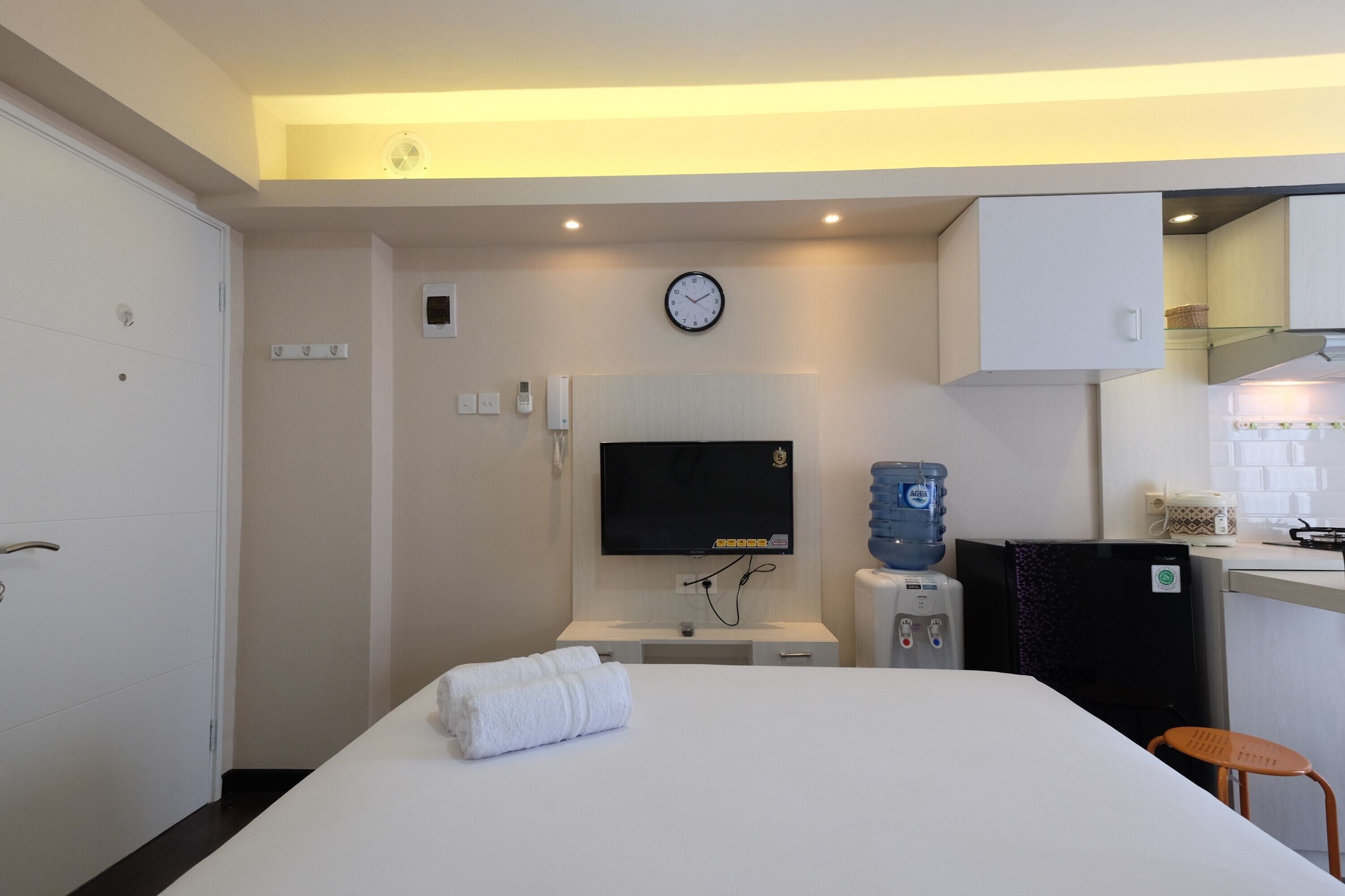 A hotel room with a bed, a TV, a water dispenser, and a kitchenette.