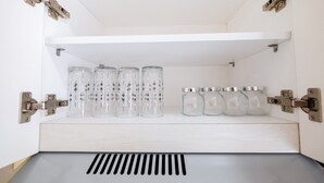 A white cabinet with multiple clear glass jars and metal lids, some with black patterns. - Newly Furnished Studio at Bassura City Apartment (Jakarta)