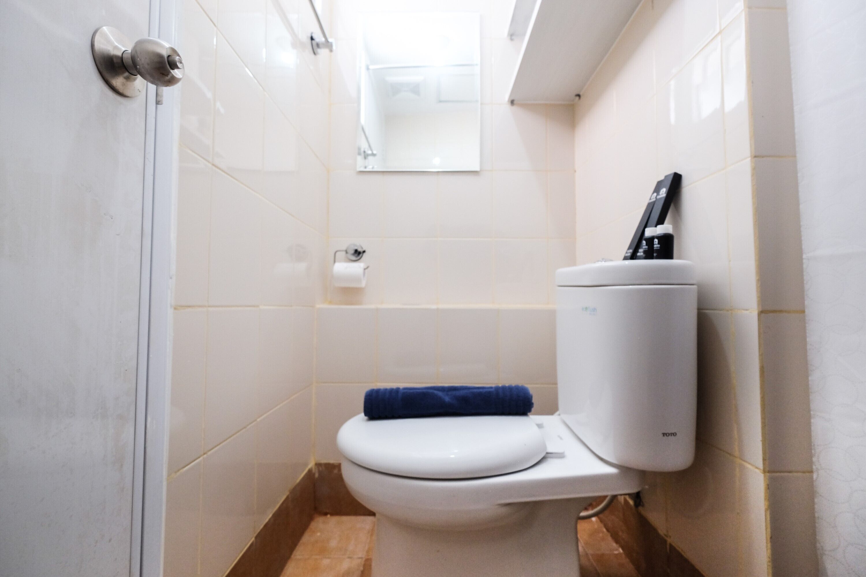 A small, modern bathroom with a white toilet, a towel on the seat, and a toilet paper holder on the wall.