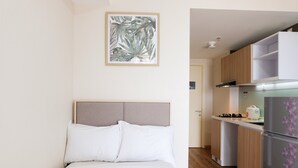 Une chambre à coucher comprenant un lit, une tête de lit et un tableau accroché au mur. À côté de la chambre se trouve une cuisine équipée de meubles en bois, d’un réfrigérateur et d’une cuisinière.