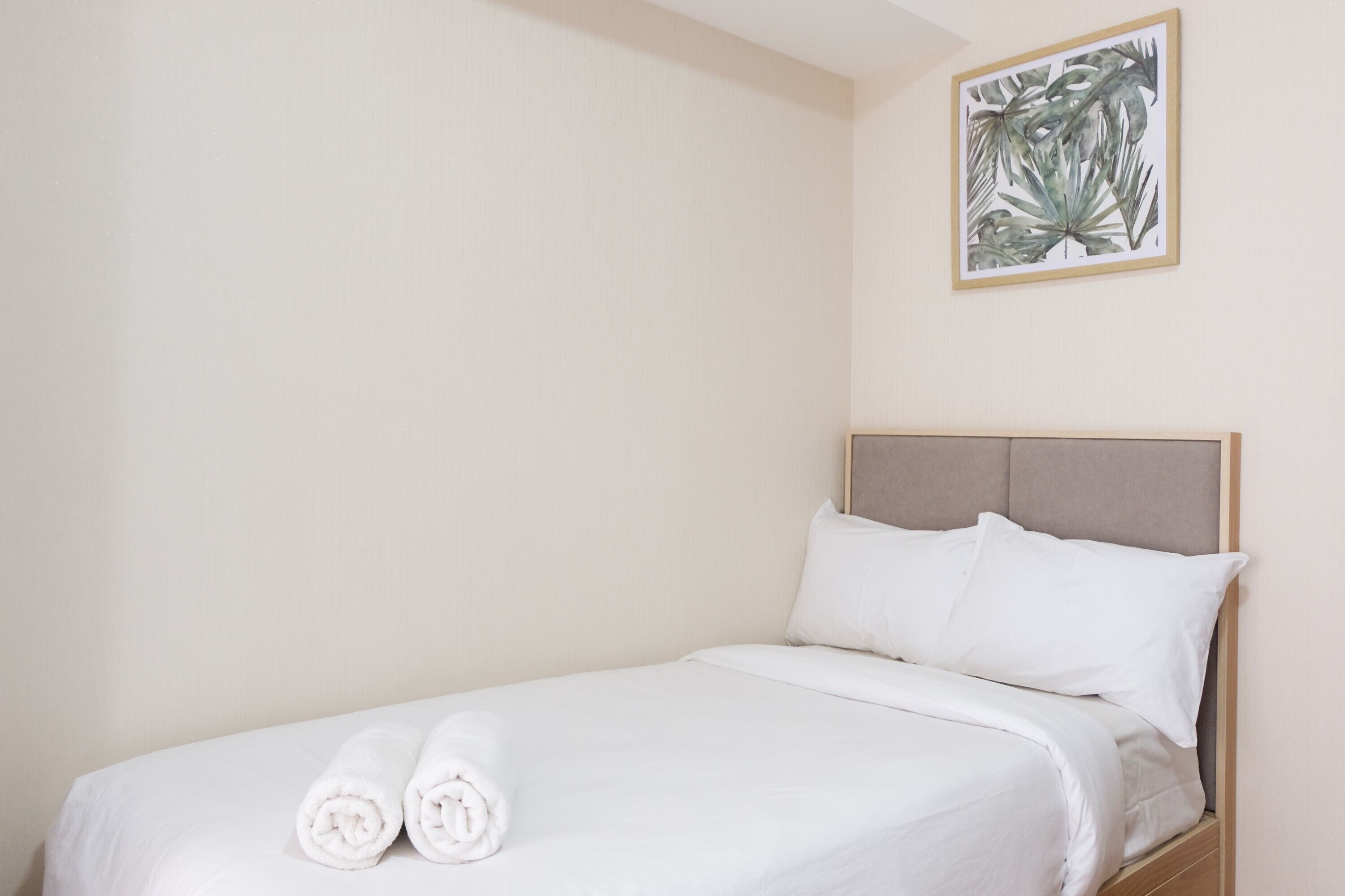 A neatly made bed with white linens and pillows, a framed botanical print on the wall, and a wooden headboard.