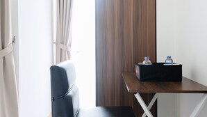 A hotel room with a wooden desk, a black leather chair, and a small black table with two water bottles. - Comfortable Studio Apartment M-Town Residence (Gading Serpong)