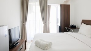 A hotel room with a bed, a TV, a desk, and curtains. - Comfortable Studio Apartment M-Town Residence (Gading Serpong)