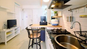 A modern kitchen with a gas stove, stainless steel sink, and bar stools. - Best Price 2BR Bassura City Apartment (Jakarta)
