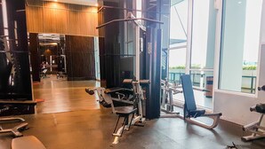 A gym with various exercise equipment, including treadmills and weight machines, and large windows offering views of the outside. - Cozy Studio Apartment at Brooklyn Alam Sutera (South Tangerang)