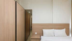 A modern hotel room with a wooden wardrobe, a wooden nightstand, and a bed with white bedding. - Cozy Studio Apartment at Brooklyn Alam Sutera (South Tangerang)