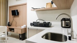 A modern kitchen with a built-in stove, a sink, a countertop, a television mounted on the wall, and a wooden shelf above the counter. - Cozy Studio Apartment at Brooklyn Alam Sutera (South Tangerang)