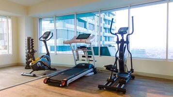 Un gimnasio con cintas de correr, elíptica y máquina de remo, amplias ventanas con vista a la ciudad.