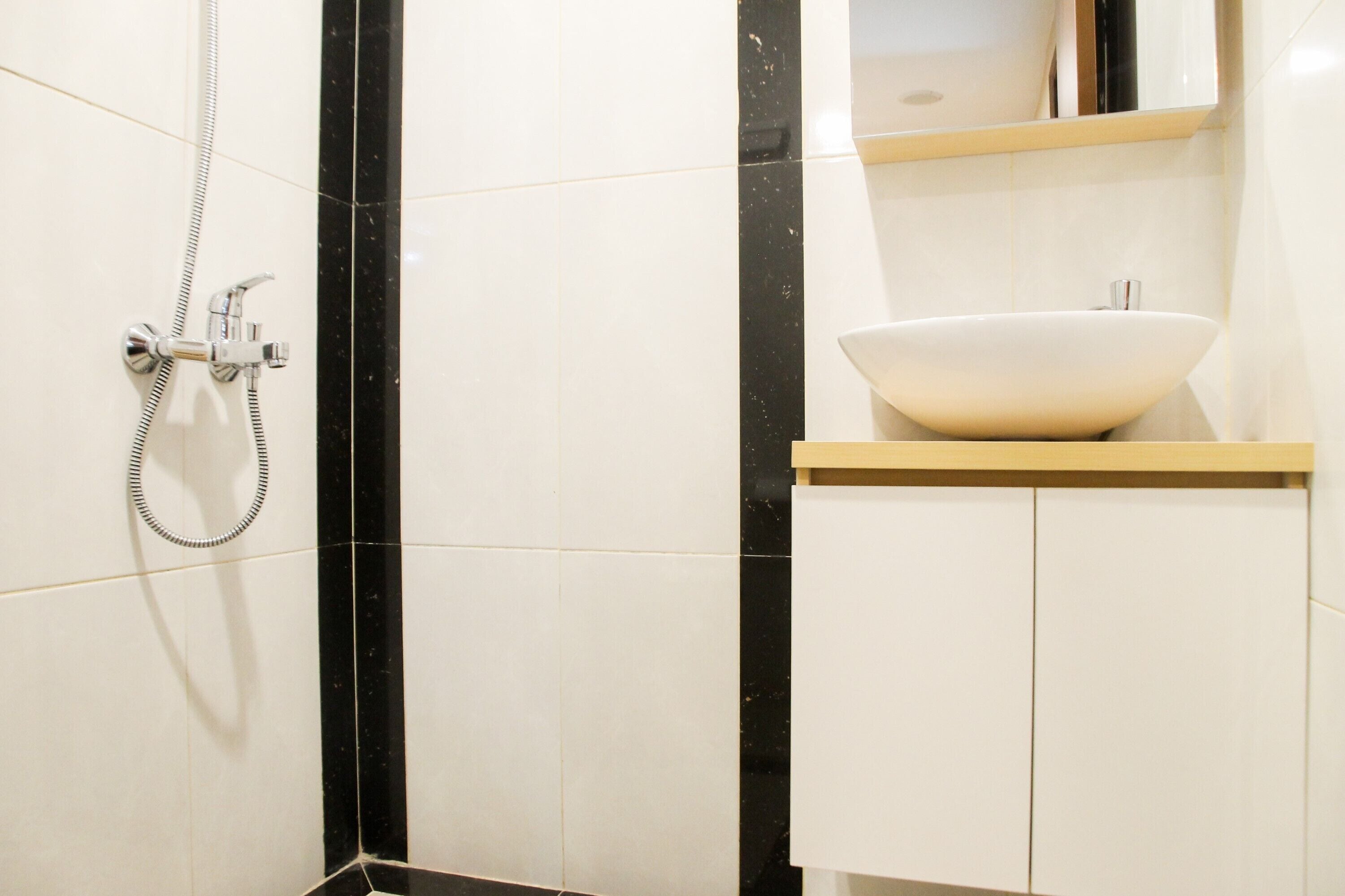 A bathroom with a white sink, black and white tiled walls, and a shower with a handheld hose.