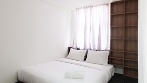 A neatly made bed with white linens and pillows, a wooden wardrobe, and sheer curtains on a window. - Modern City View Studio Apartment at Tuscany Residences (South Tangerang)
