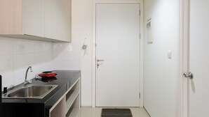 A kitchen with a sink, a red stove, and white cabinets. - Modern City View Studio Apartment at Tuscany Residences (South Tangerang)