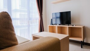 A modern living room with a sofa, a TV on a wooden stand, and a large window with curtains. - Highest Value 1BR Apartment at Asatti Vanya Park (Pagedangan)