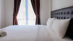 A hotel room with a large bed, white linens, a tufted headboard, and brown curtains. - Highest Value 1BR Apartment at Asatti Vanya Park (Pagedangan)