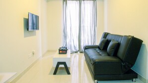 A living room with a black leather sofa, a small white table, and a flat-screen TV mounted on the wall. - Wonderful 2BR at Gold Coast Apartment Pantai Indah Kapuk (Jakarta)
