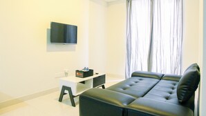 A modern living room with a black leather sofa, a small white table, and a flat-screen TV mounted on the wall. - Wonderful 2BR at Gold Coast Apartment Pantai Indah Kapuk (Jakarta)