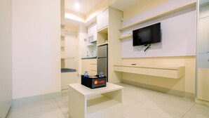 Une chambre d’hôtel moderne dotée d’un téléviseur à écran plat fixé au mur, d’une petite table blanche avec une trousse de toilette et d’un coin cuisine intégré.