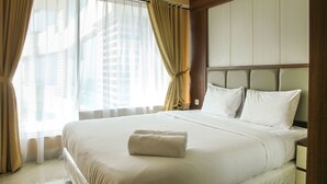 A hotel room with a large bed, beige curtains, and a view of buildings through the window. - Modern 2BR Grand Kamala Lagoon Apartment (Bekasi)