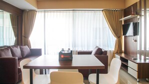 A modern hotel room with a dining area, a sofa, a TV, and a minibar. - Modern 2BR Grand Kamala Lagoon Apartment (Bekasi)