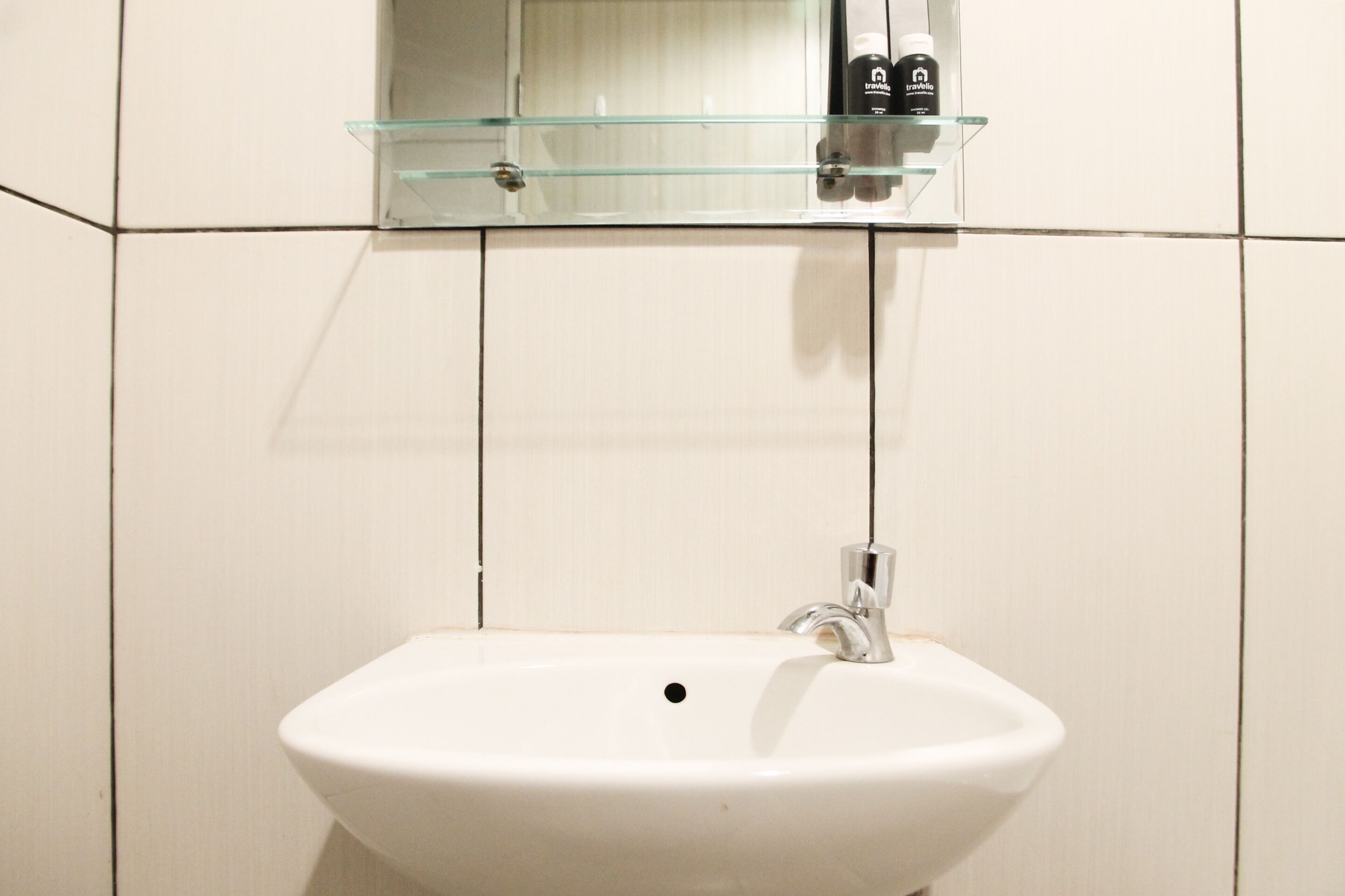 A bathroom with a white sink, a glass shelf above it, and a mirror.