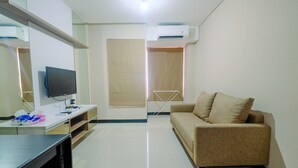 A modern living room with a flat-screen TV, a sofa, a desk with a computer, and a built-in wardrobe. - Comfy 2BR Apartment at Nifarro Park Pasar Minggu (Jakarta)