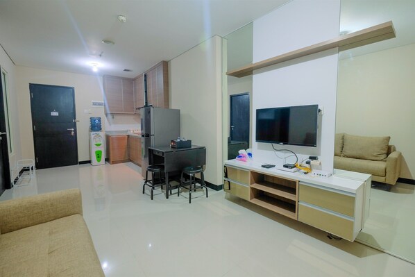 A modern living room with a sofa, a TV, a small dining area, and a kitchenette.