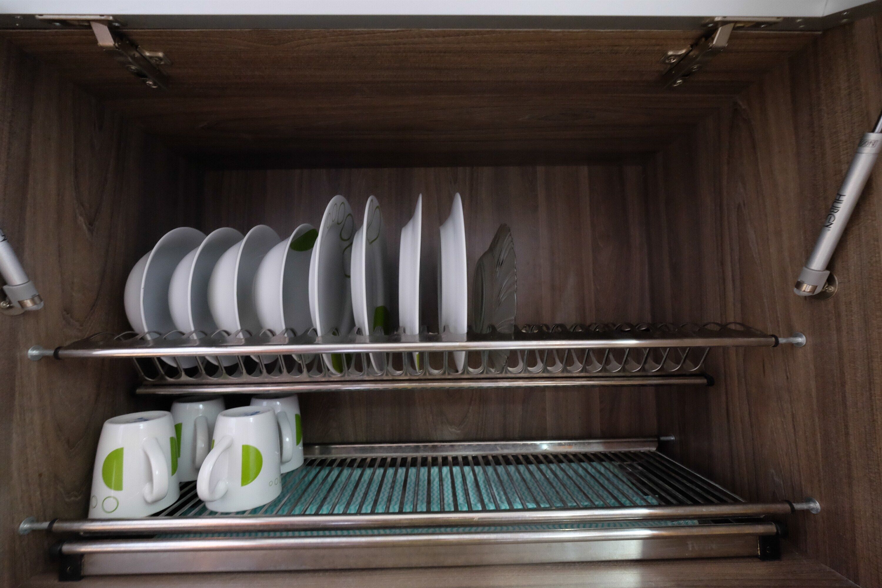 A kitchen with wooden cabinets, a stainless steel sink, and a dish rack with plates and cups.