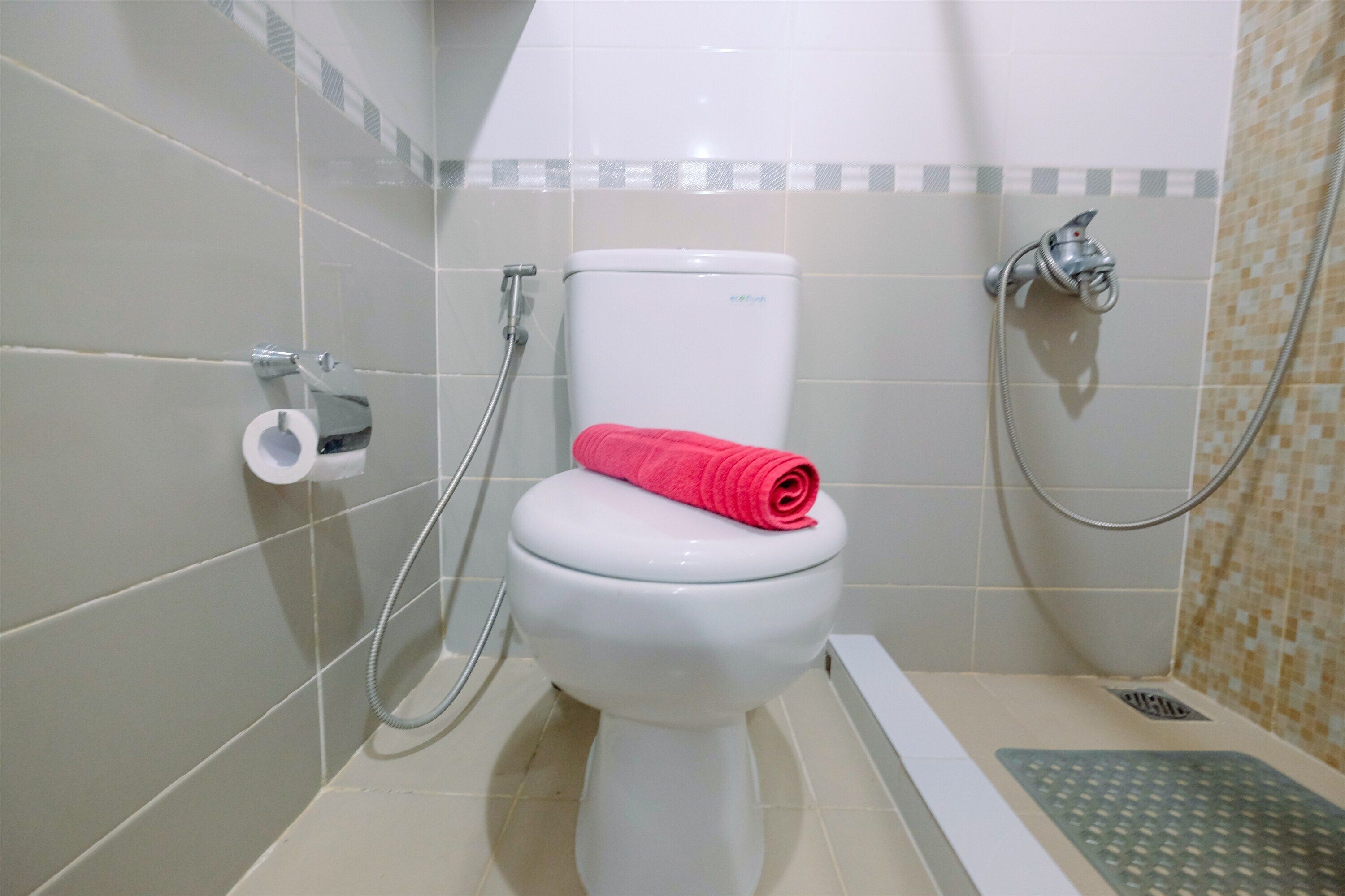 Une salle de bain avec des toilettes blanches, une douche et un porte-rouleau de papier toilette.