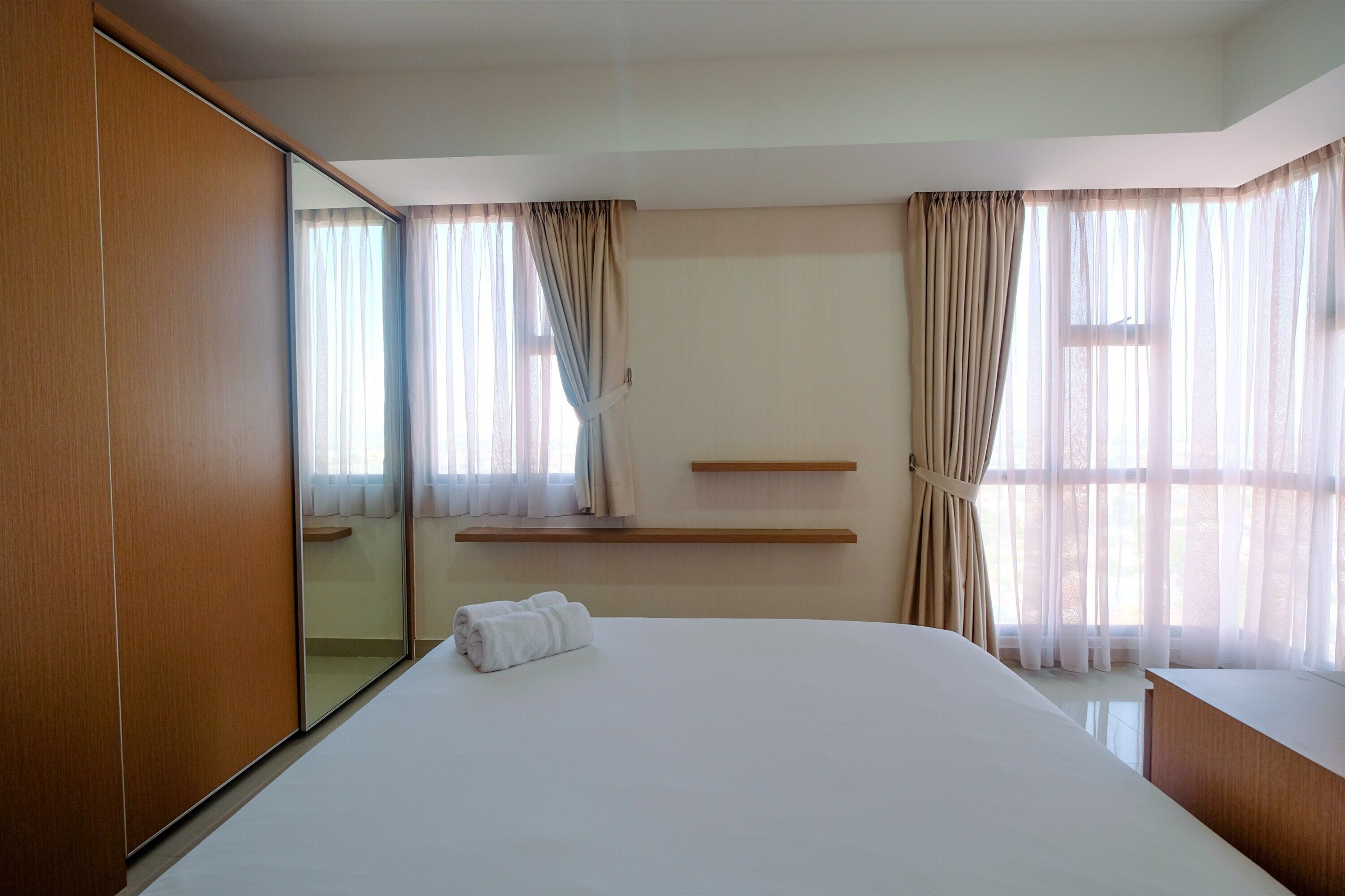 Habitación de hotel con una cama grande, un armario de madera, un espejo, una mesita de noche y una ventana con cortinas.