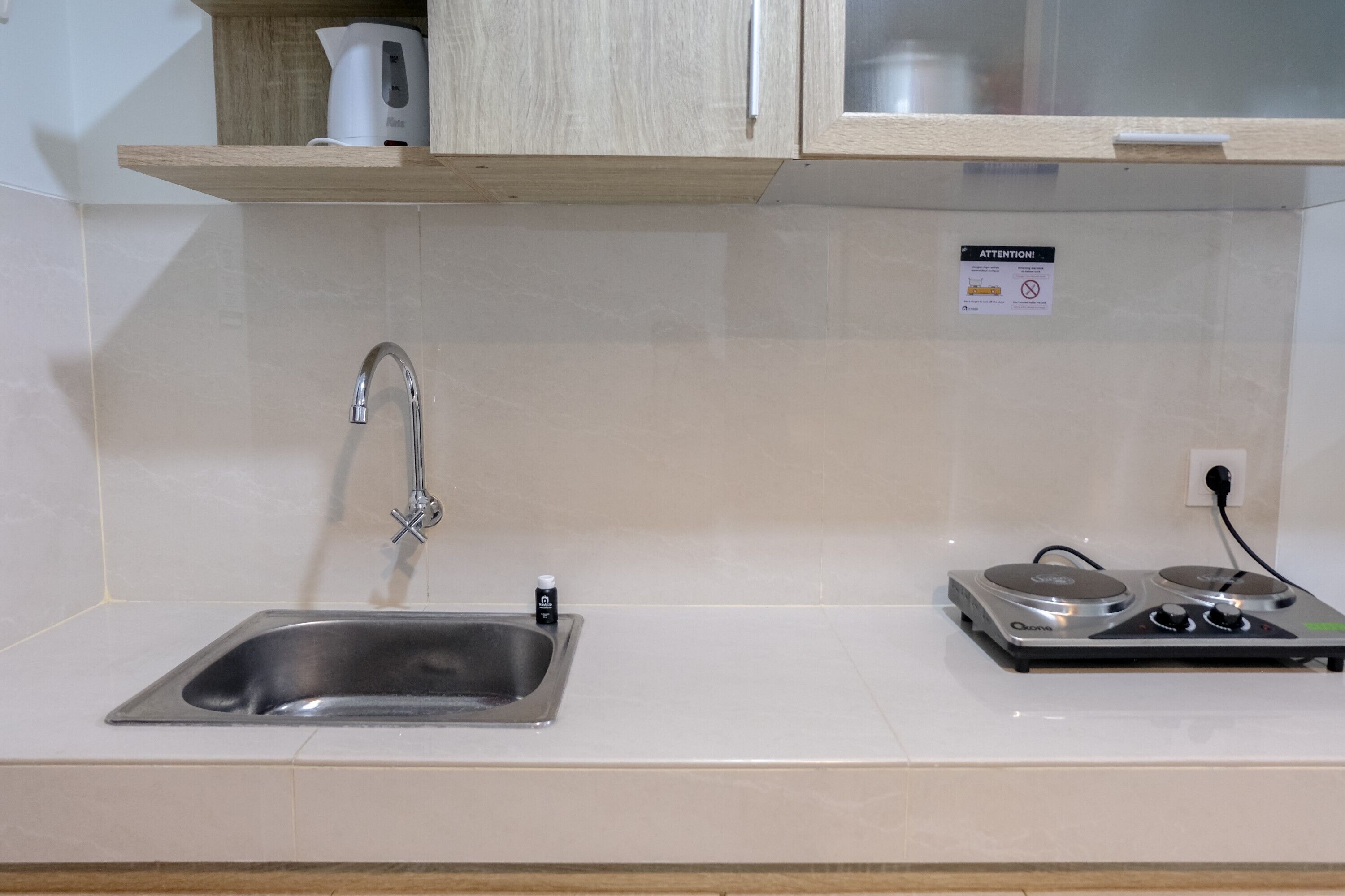 Una cocina con un lavamanos de acero inoxidable, una tetera y una cafetera sobre un estante de madera.