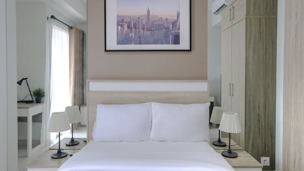 Une chambre d’hôtel avec un grand lit, deux tables de chevet avec des lampes, un tableau représentant un paysage urbain encadré au mur et une armoire.