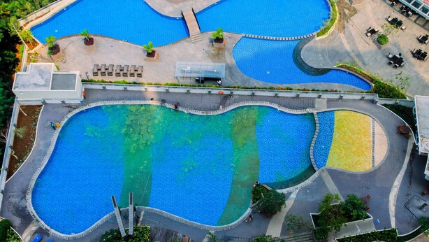 An aerial view of a hotel with multiple interconnected swimming pools, a covered seating area, and a landscaped garden. - Modern 2BR at The Wave Epicentrum Apartment near Kuningan (Jakarta)